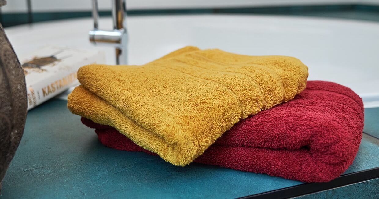 To håndklæder i orange og rød, der ligger ved et spaområde i et badeværelse. Teksturen er blød.