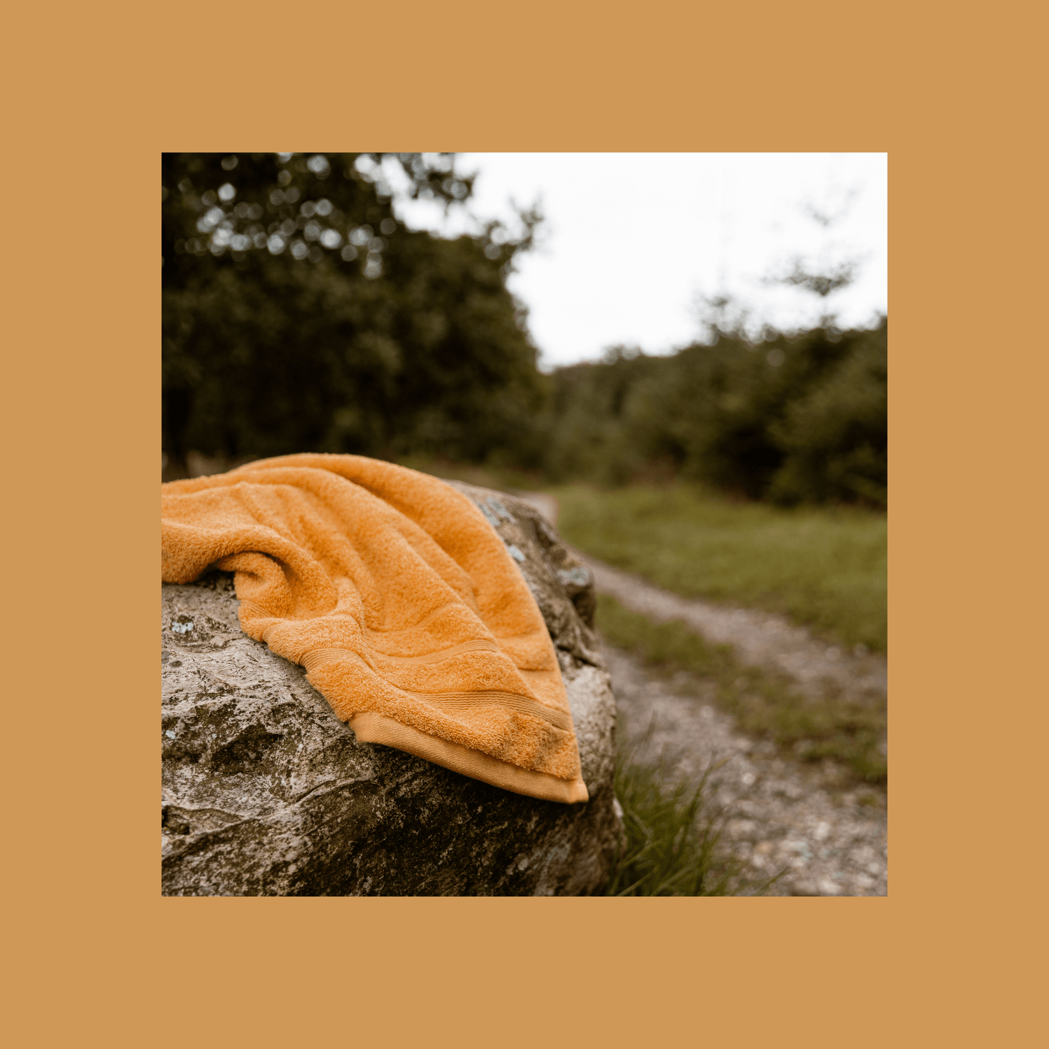 Orange håndklæde i økologisk bomuld placeret på en sten ude i naturen. 