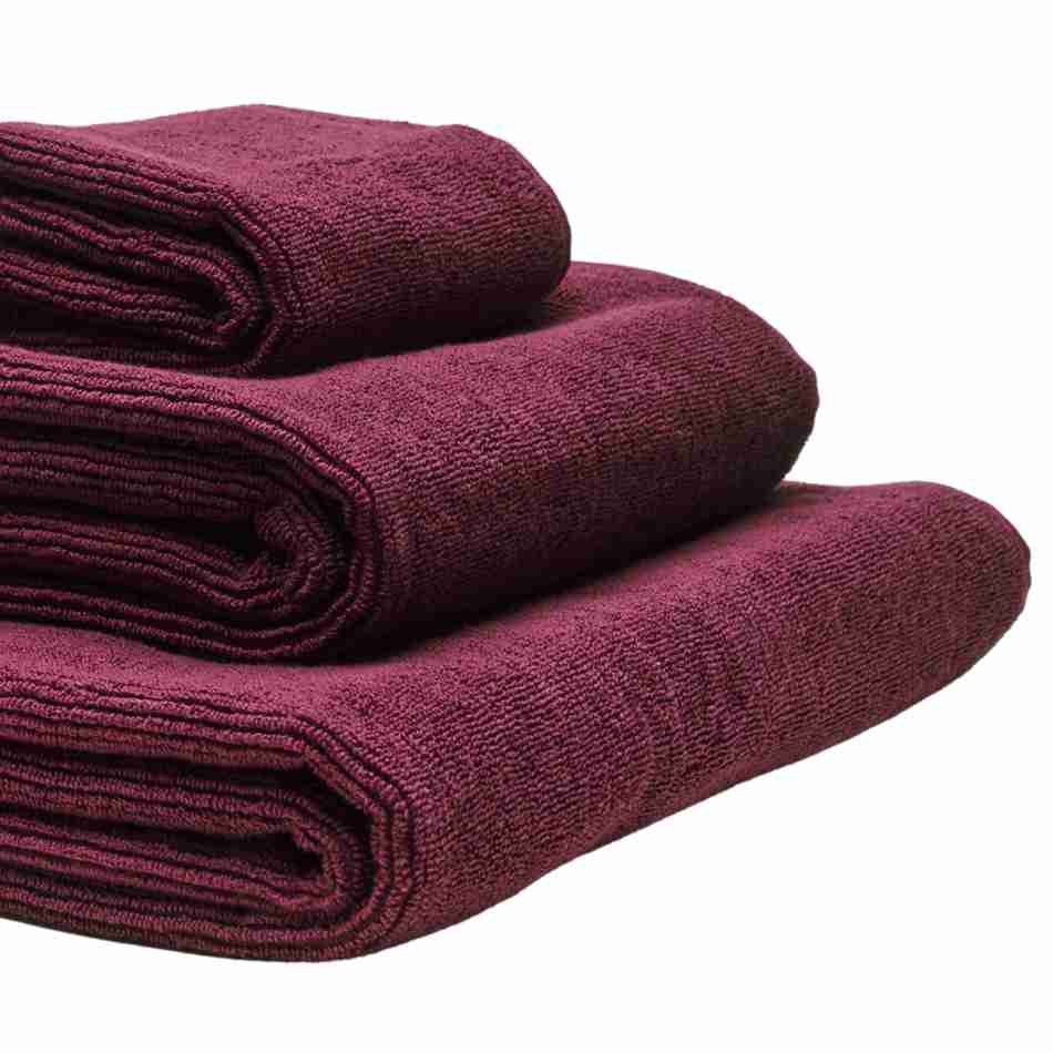 Tre håndklæder i økologisk bomuld og af forskellig størrelser stablet oven på hinanden. Farven på håndklæderne er bordeaux.