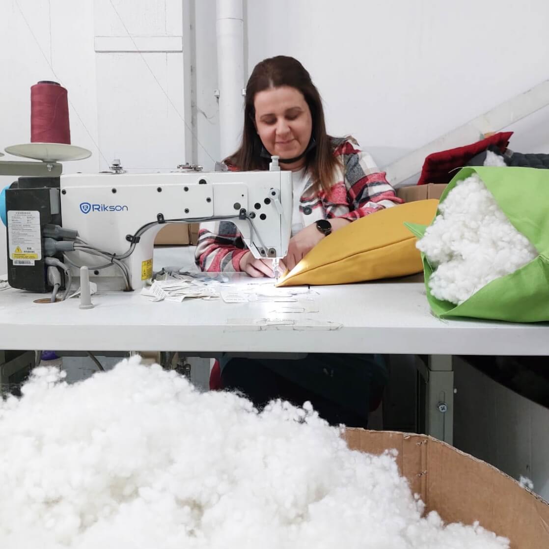 Smilende kvinde der syer økologiske bomuldsprodukter på en symaskine