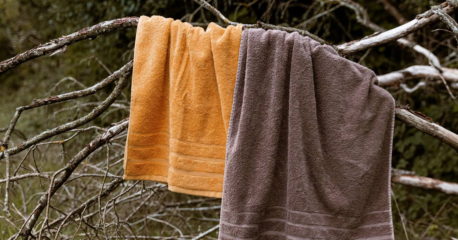 To håndklæder i orange og brun farve, der hænger på en gren i naturlige omgivelser