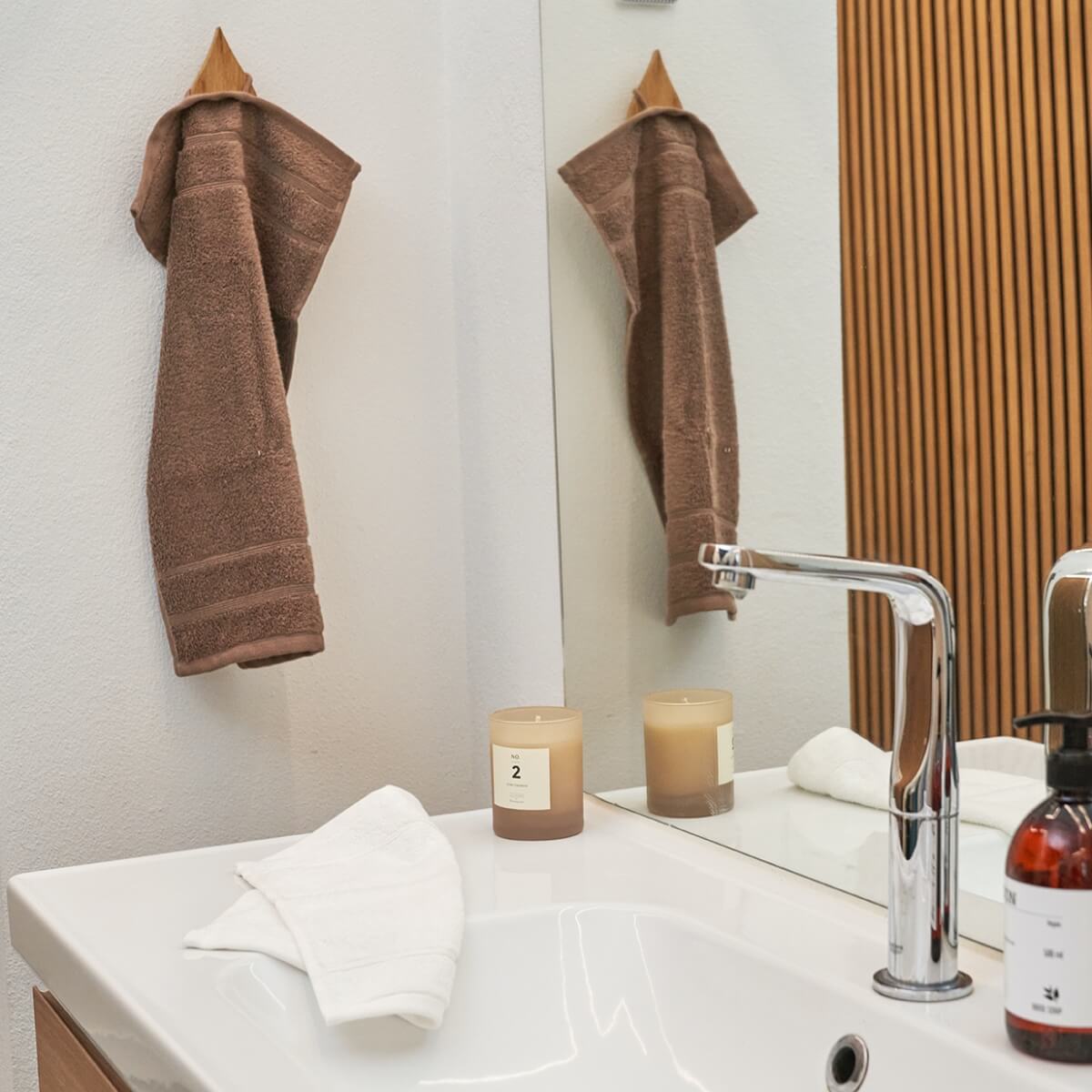 Vask med økologiske håndklæder i henholdsvis brun og hvid farve. Omkring håndklæderne er et duftlys og en sæbe.