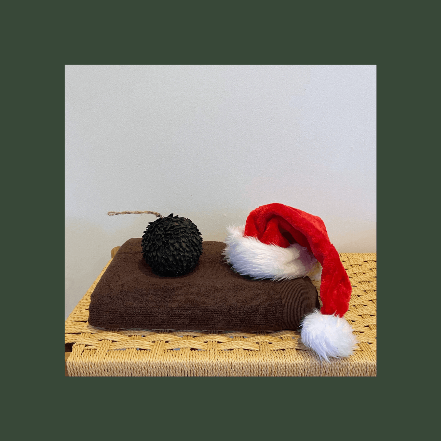 Julebillede af brunt bomuldshåndklæde på træbænk med nissehue og grankogle ovenpå