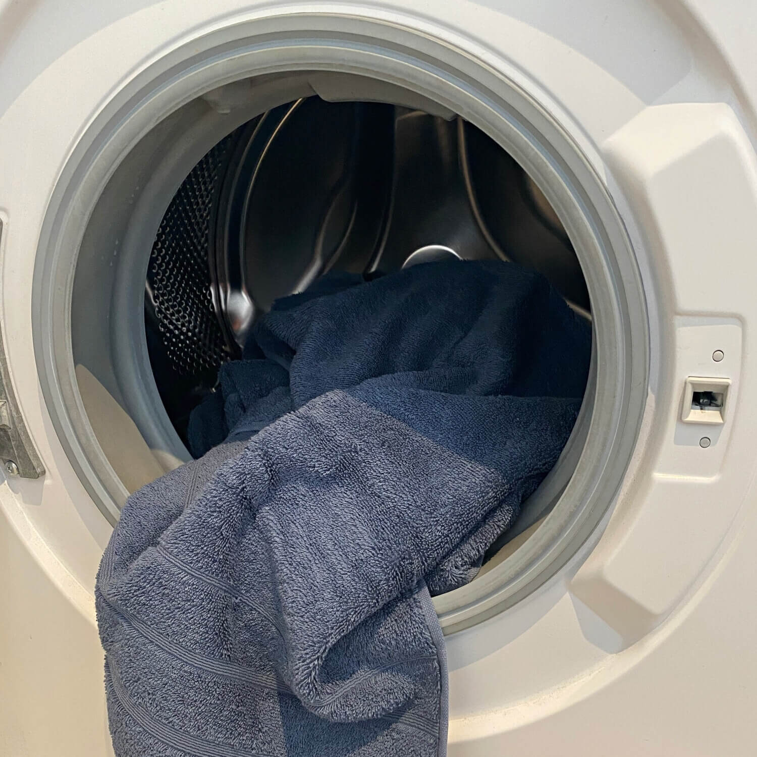 Et blåt håndklæde i en hvid vaskemaskine med åben låge