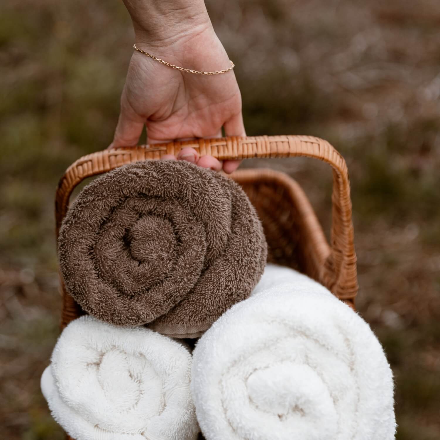 To hvide håndklæder og et brunt håndklæde i en brun, vævet kurv, der bliver båret af hånden på en person