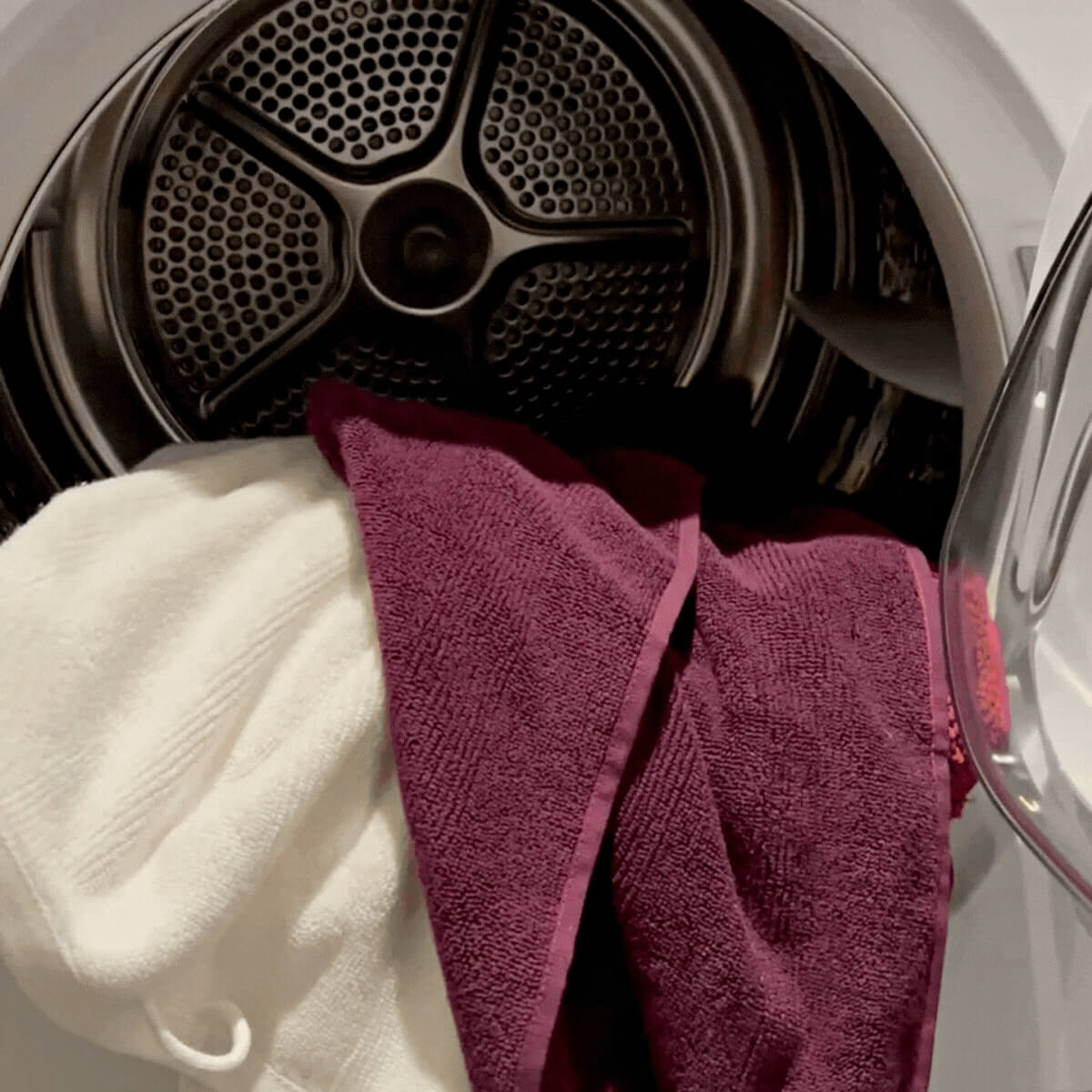 Økologiske håndklæder ligger i vaskemaskinen. Der er to håndklæder i farven hvid og bordeaux. 