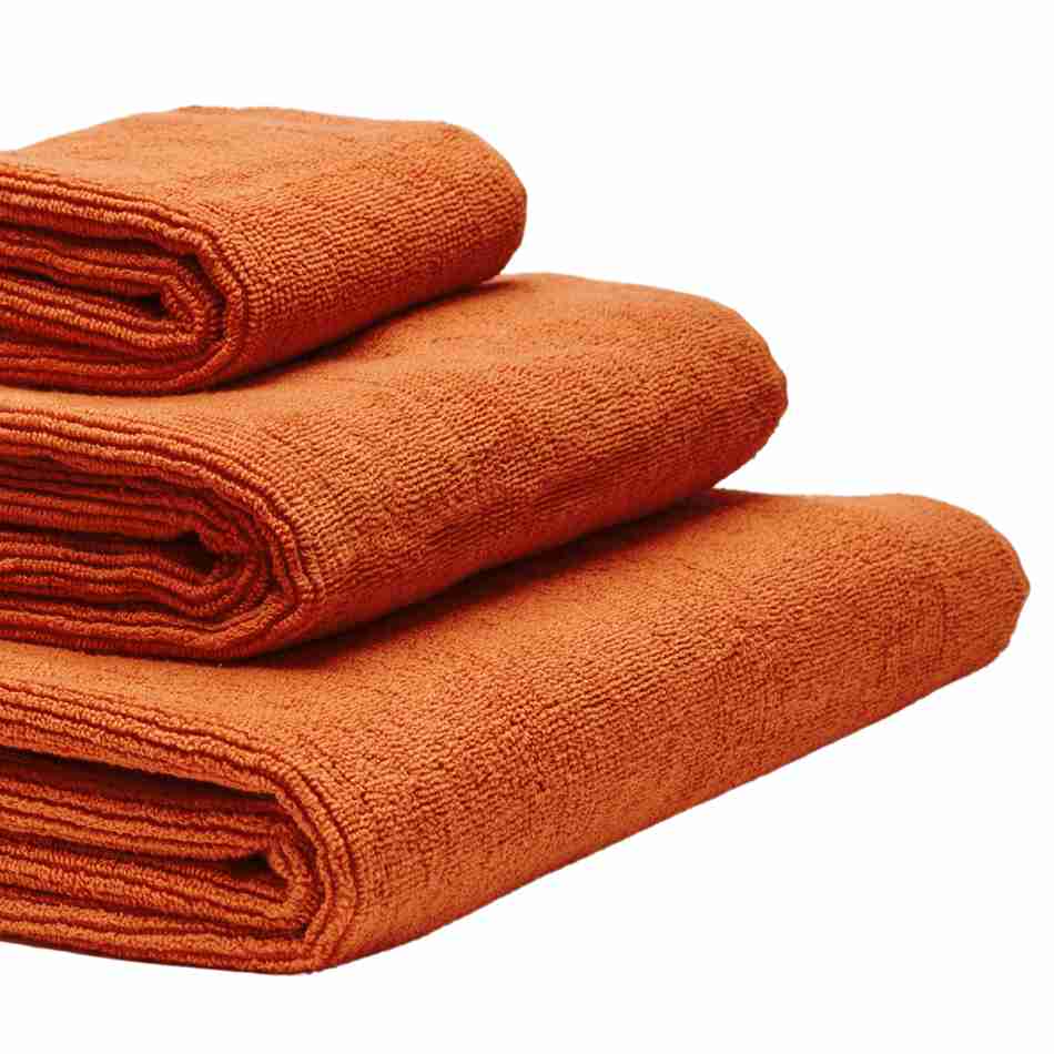 Tre håndklæder i økologisk bomuld og af forskellig størrelser stablet oven på hinanden. Farven på håndklæderne er orange.