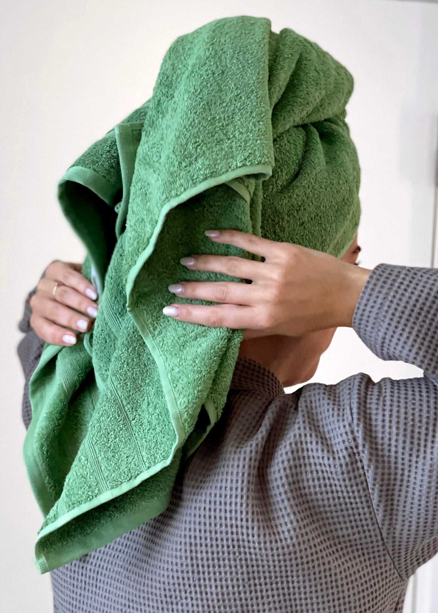 Kvinde har vinklet et grønt håndklæde om hovedet. Hun er iklædt en grå økologisk badekåbe.