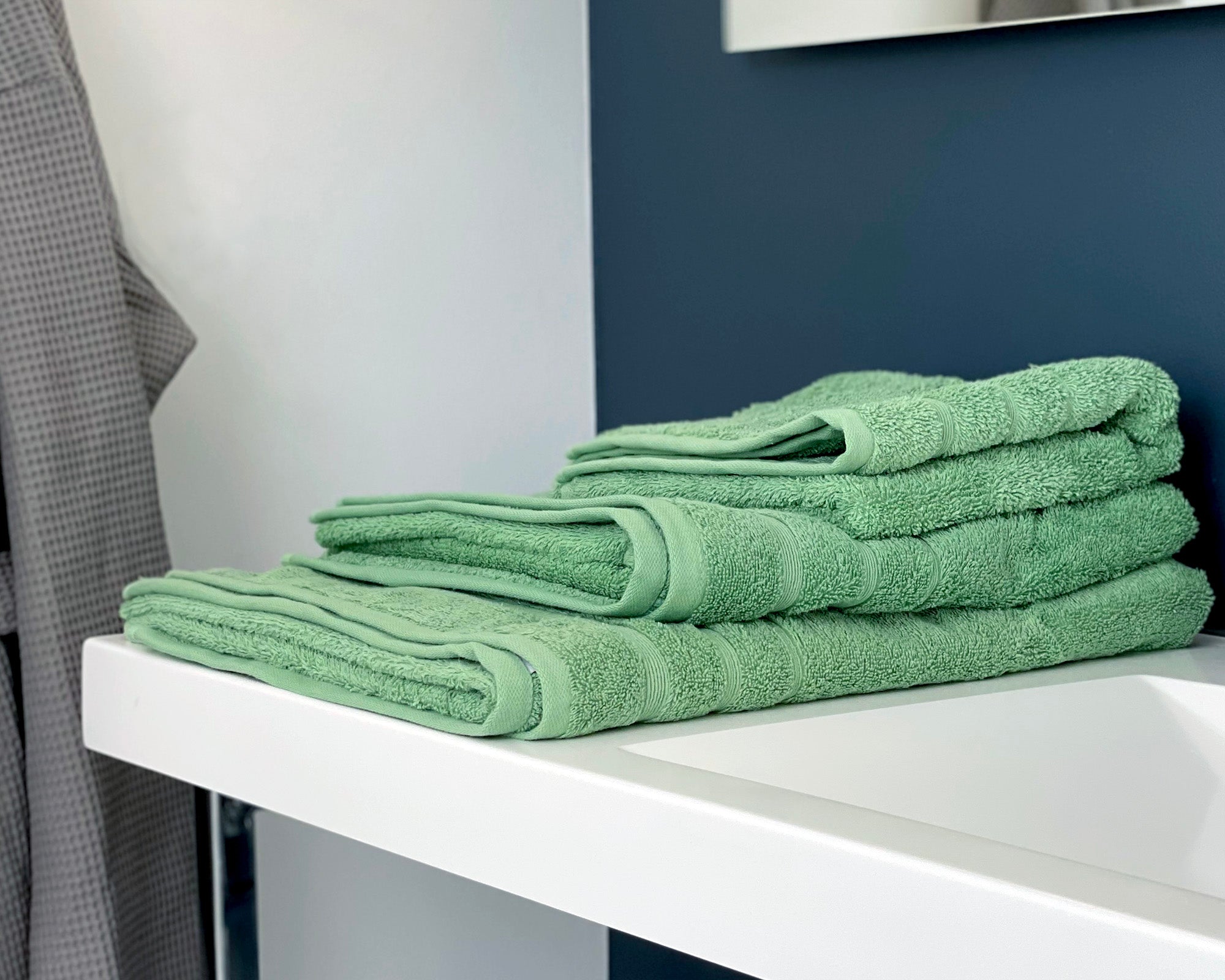 Tre økologiske grønne håndklæder ligger på vasken i et badeværelse. 