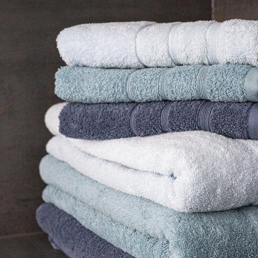 Seks håndklæder stablet oven på hinanden. Farverne er blå, mørkeblå og hvid. 