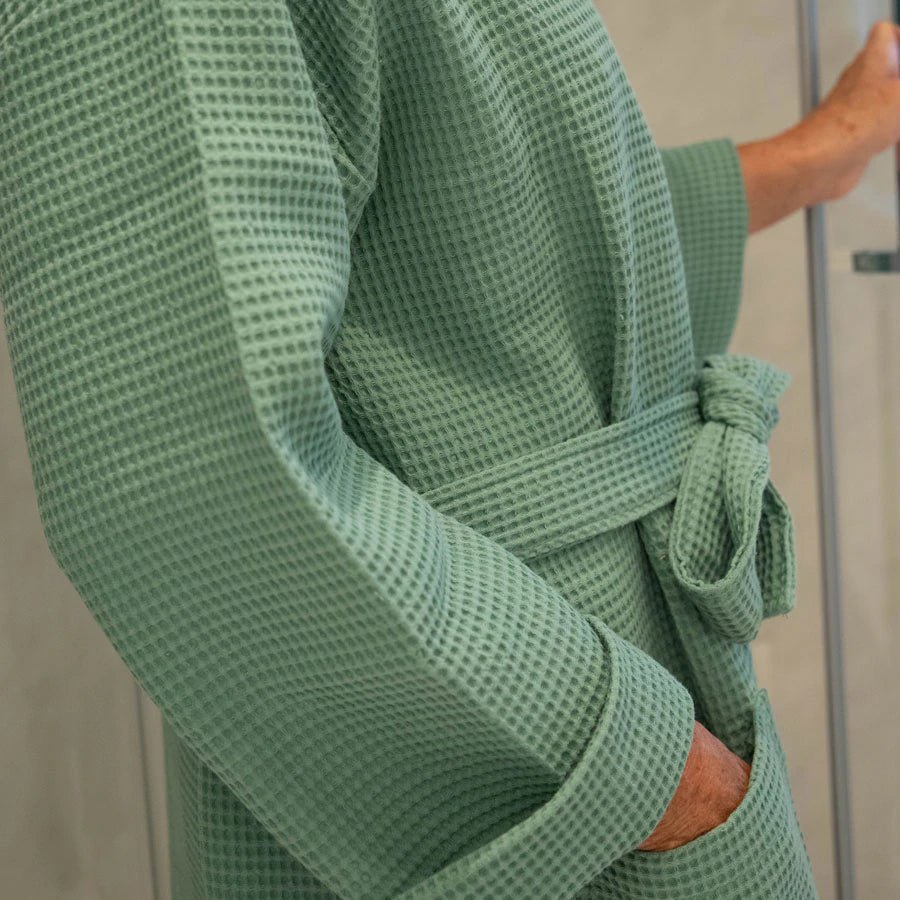 En kvinde har en økologisk badekåbe på i farven grøn eller grasgrøn.
